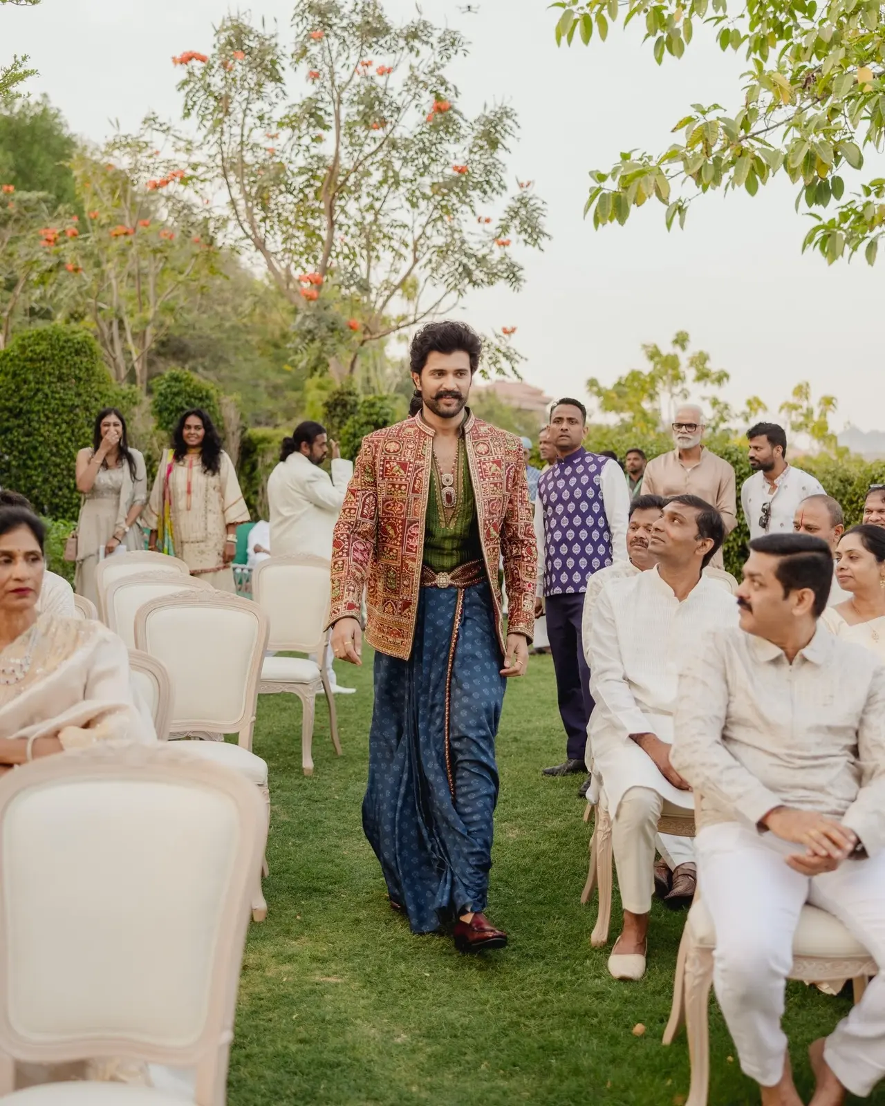For the ceremony, the couple coordinated their outfits in richly embroidered traditional ensembles by Torani. Vijay wore a deep blue silk dhoti-style bottom paired with a green kurta and a heavily embroidered jacket. 